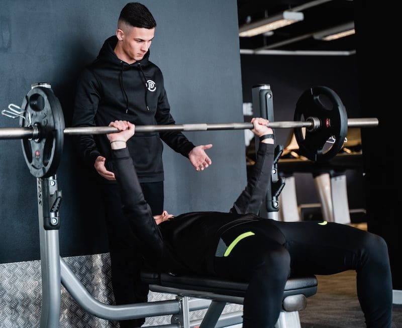 personal trainer with client on bench press